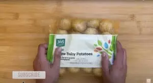 Hands holding a bag of 365 Organic Yellow Baby Potatoes on a wooden surface.